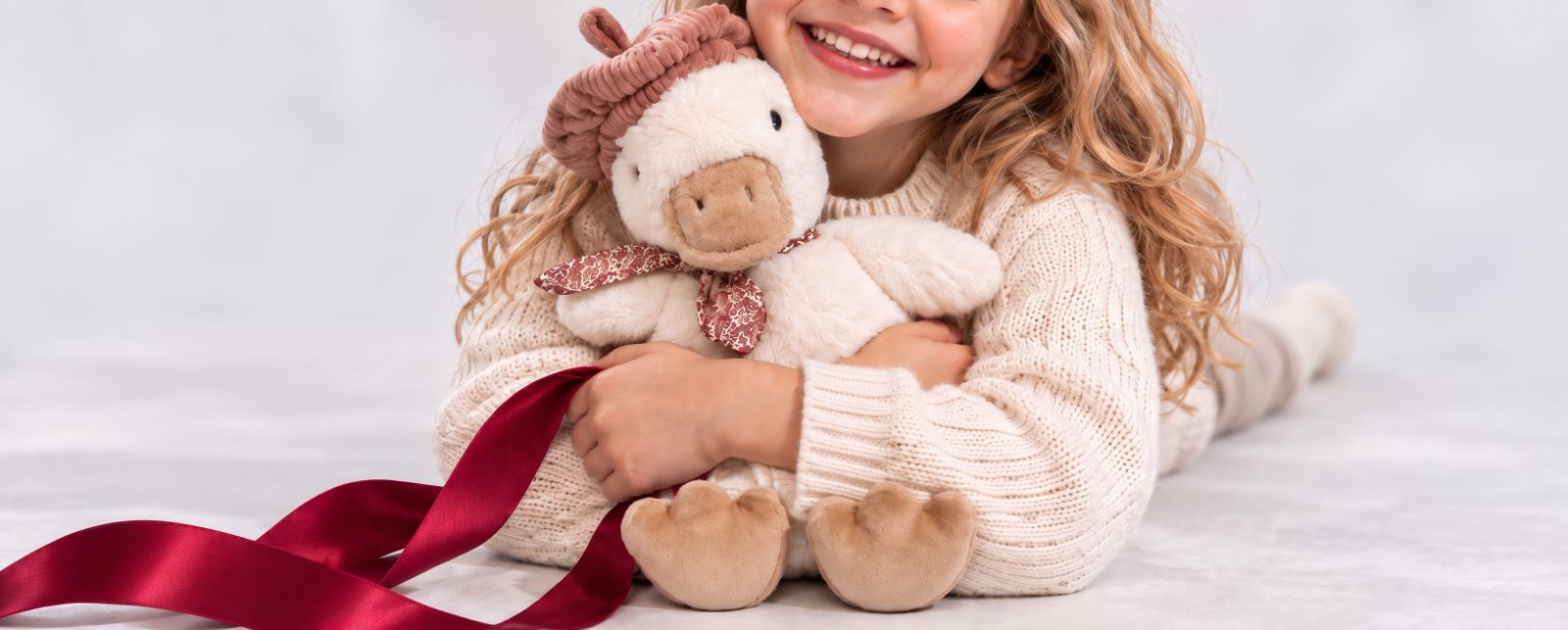 Child hugging a soft toy duck with a red ribbon