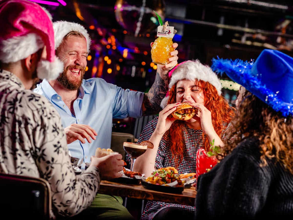 Friends in Christmas hats with food and cocktails at Boom Battle Bar