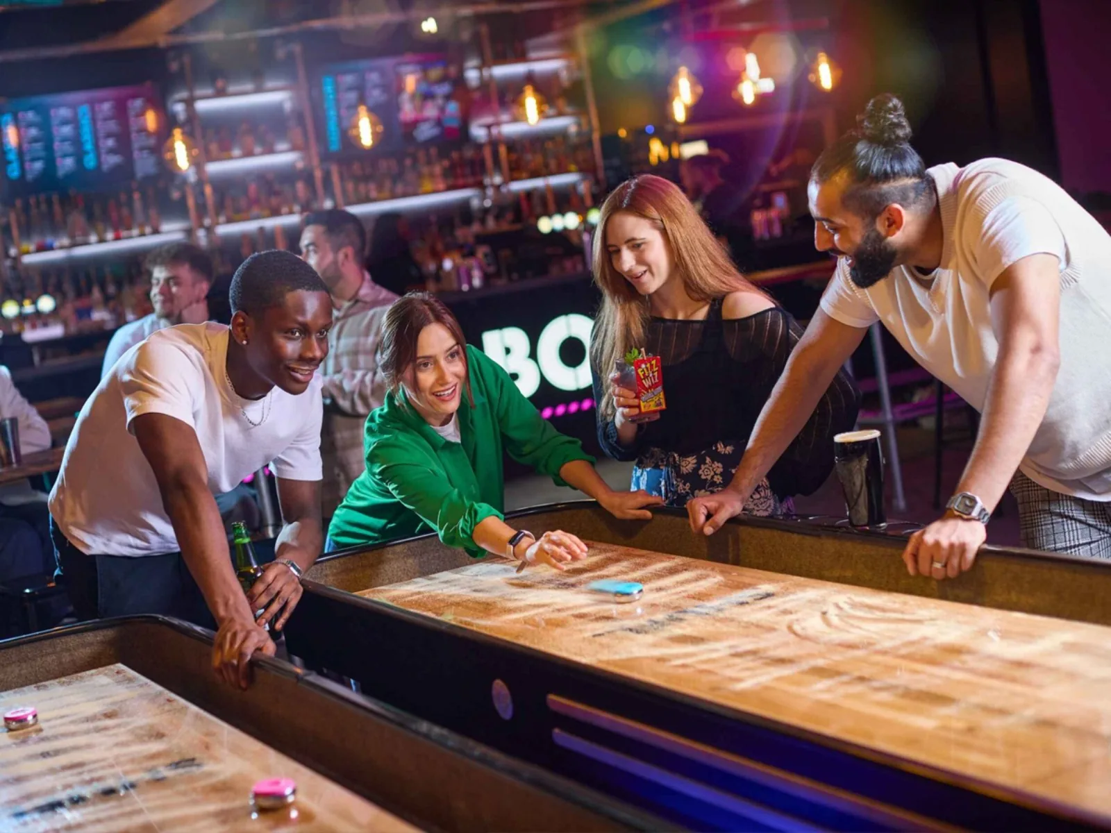 Four friends playing shuffleboard with drinks at Boom Battle Bar